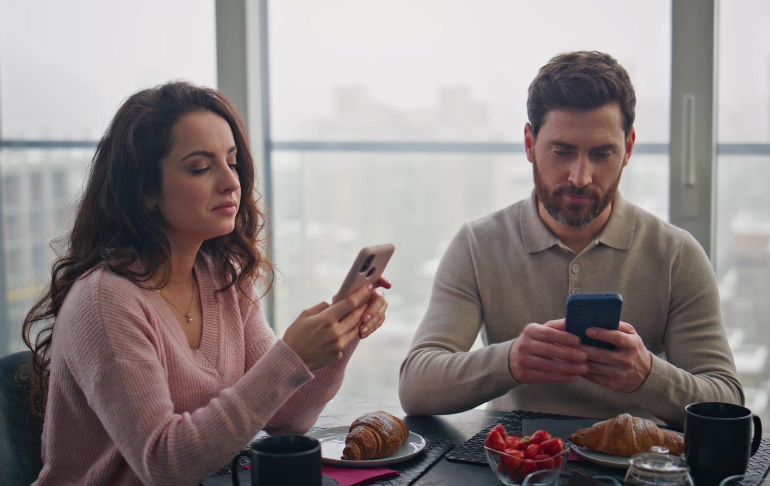 A couple both staring at their phone at the table